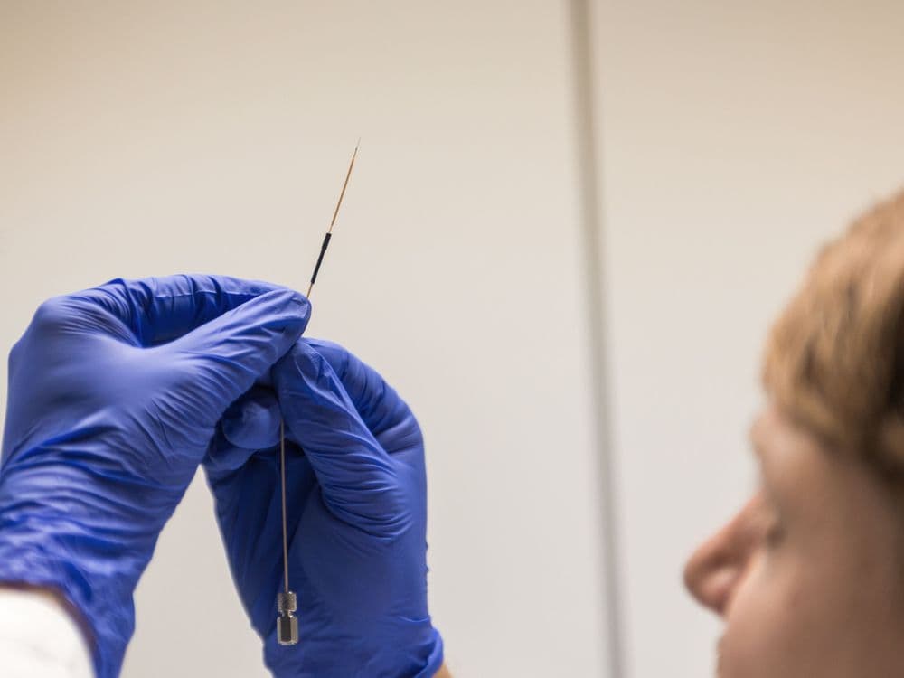 Person in blue gloves carefully holds a long, thin medical device with a small loop.