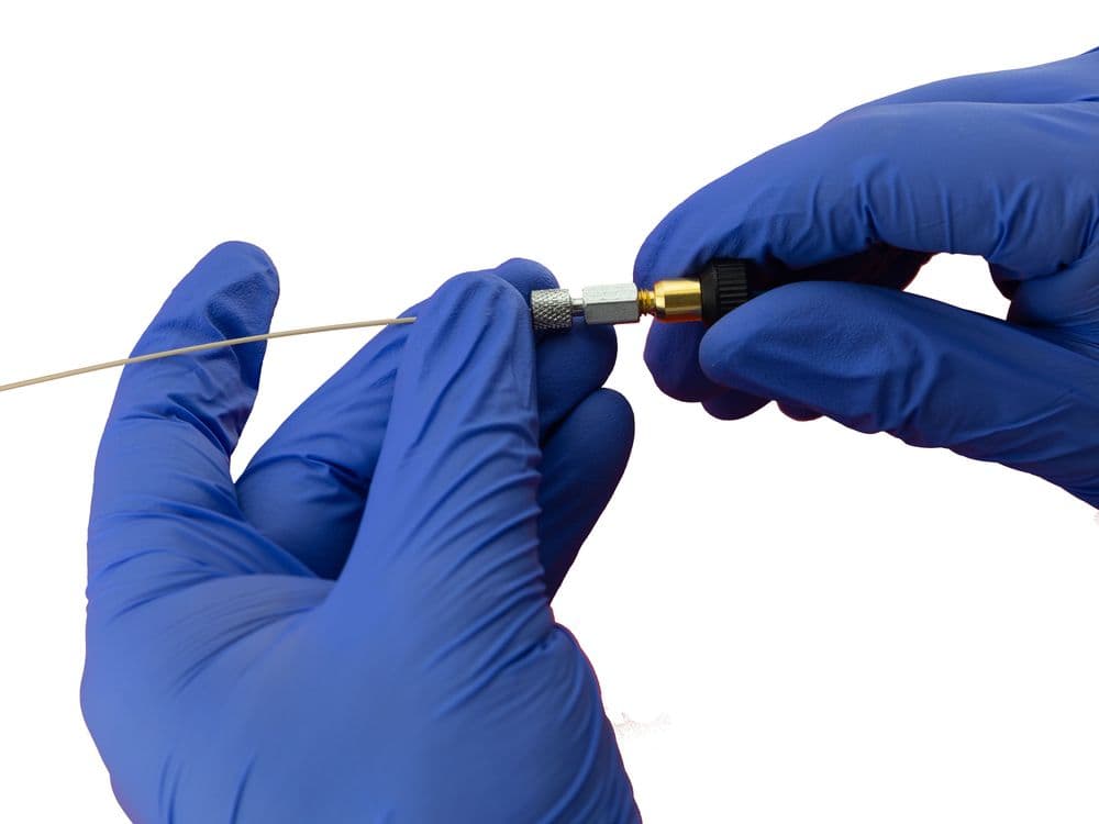 Hands in blue gloves carefully assembling a small metallic component with a black end.